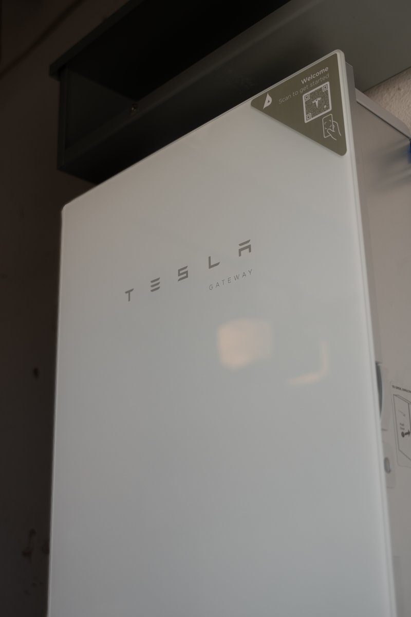 A home battery mounted on an exterior wall beside a garage