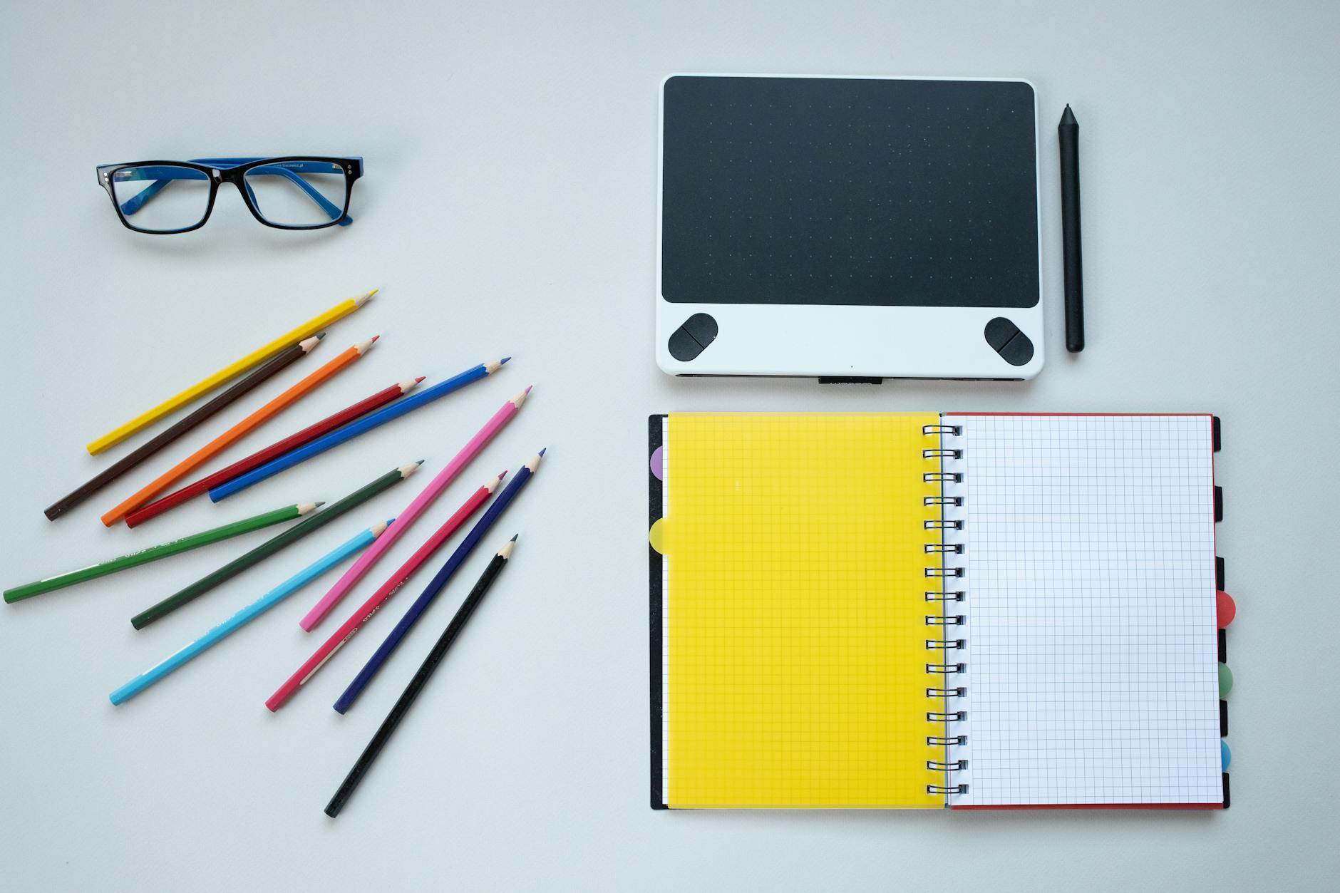 An overhead shot of colorful textbooks, a laptop, and a notepad arranged on a clean wooden school desk.