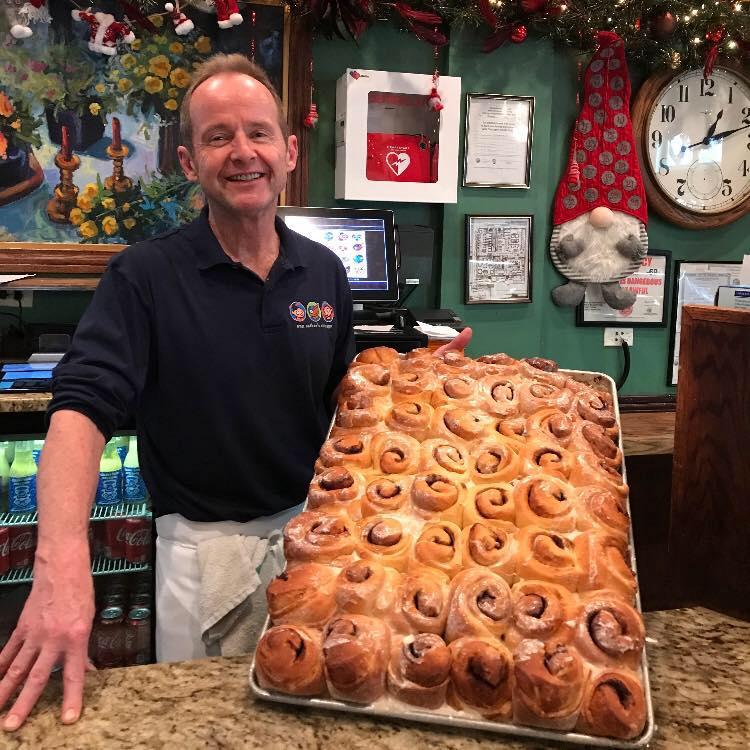 Tom Tunny holding up a large sheet of cinnamon rolls in the Ann Sather restuarant