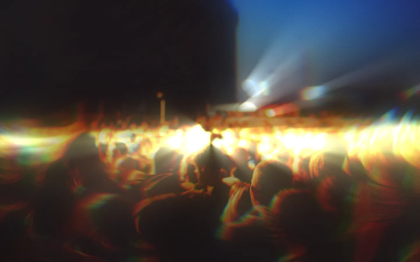 Blurry, abstract view of a concert crowd illuminated by bright stage lights with a glitchy chromatic effect.