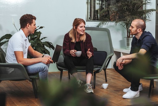 Das Layer Team, bestehend aus zwei Männer und einer Frau, sitzt im modernen Büro auf der Couch und redet bei Kaffee miteinander.