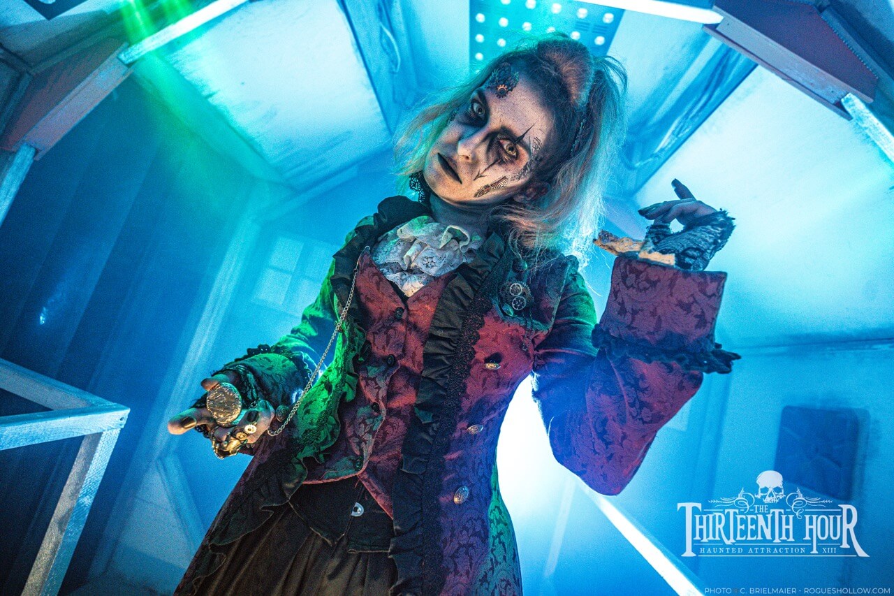 Costumed scare actor holding a pocket watch under bright blue lights