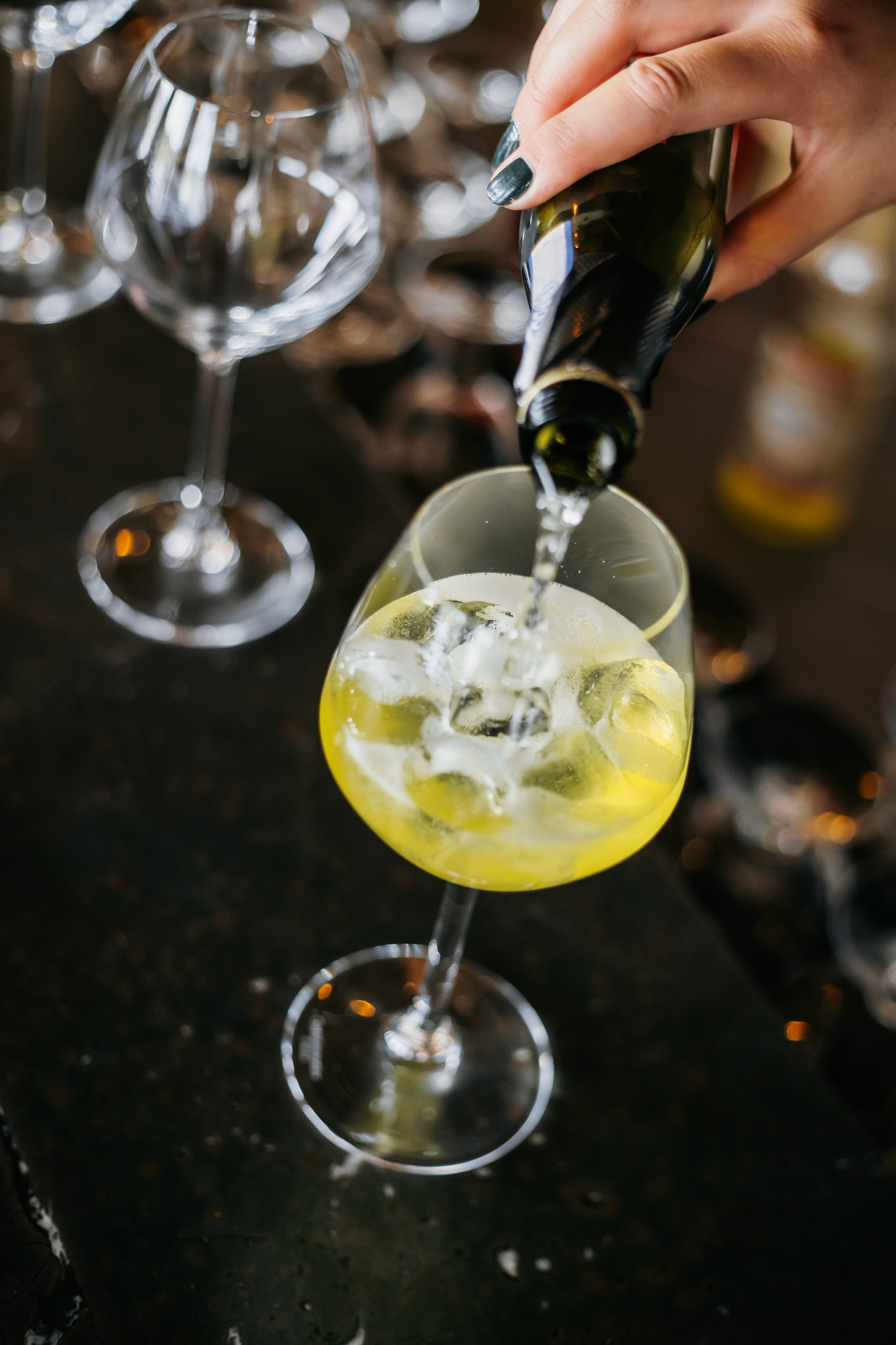White wine being poured into an ice-filled glass among stemware