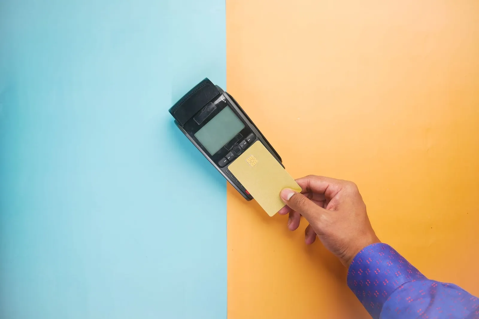 A hand tapping a card on a payment terminal against a blue and orange background
