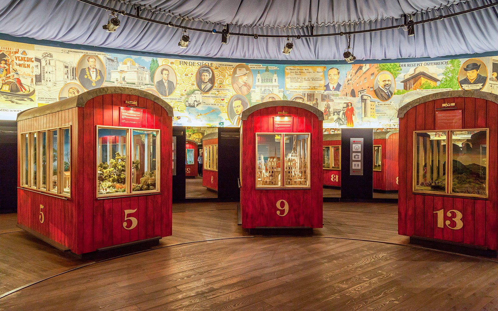 Pod pameran merah di Roda Sejarah 'Panorama' dengan mural bersejarah di latar belakang.