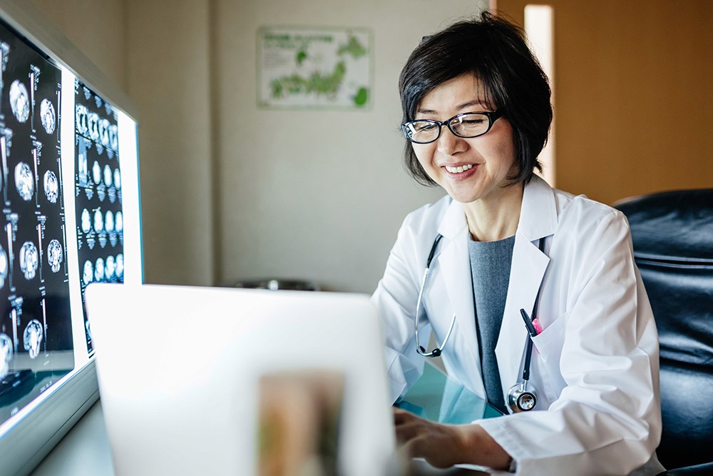 Doctor at desk reviewing work on a laptop