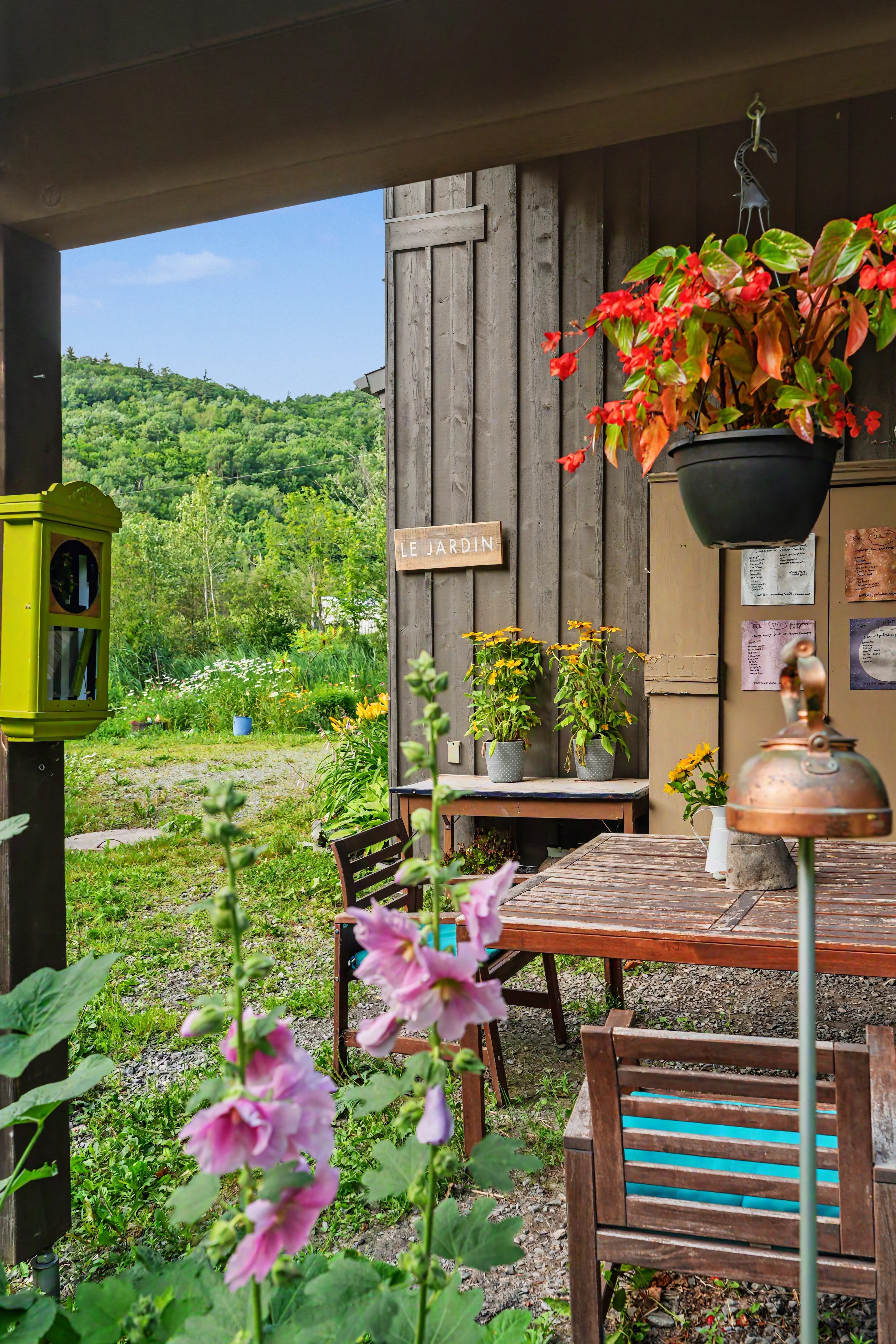 Jardin du gîte R112 Nord à Austin, avec vue sur les montagnes verdoyantes sous un ciel bleu parsemé de nuages, panneau en bois « Le Jardin » au premier plan.