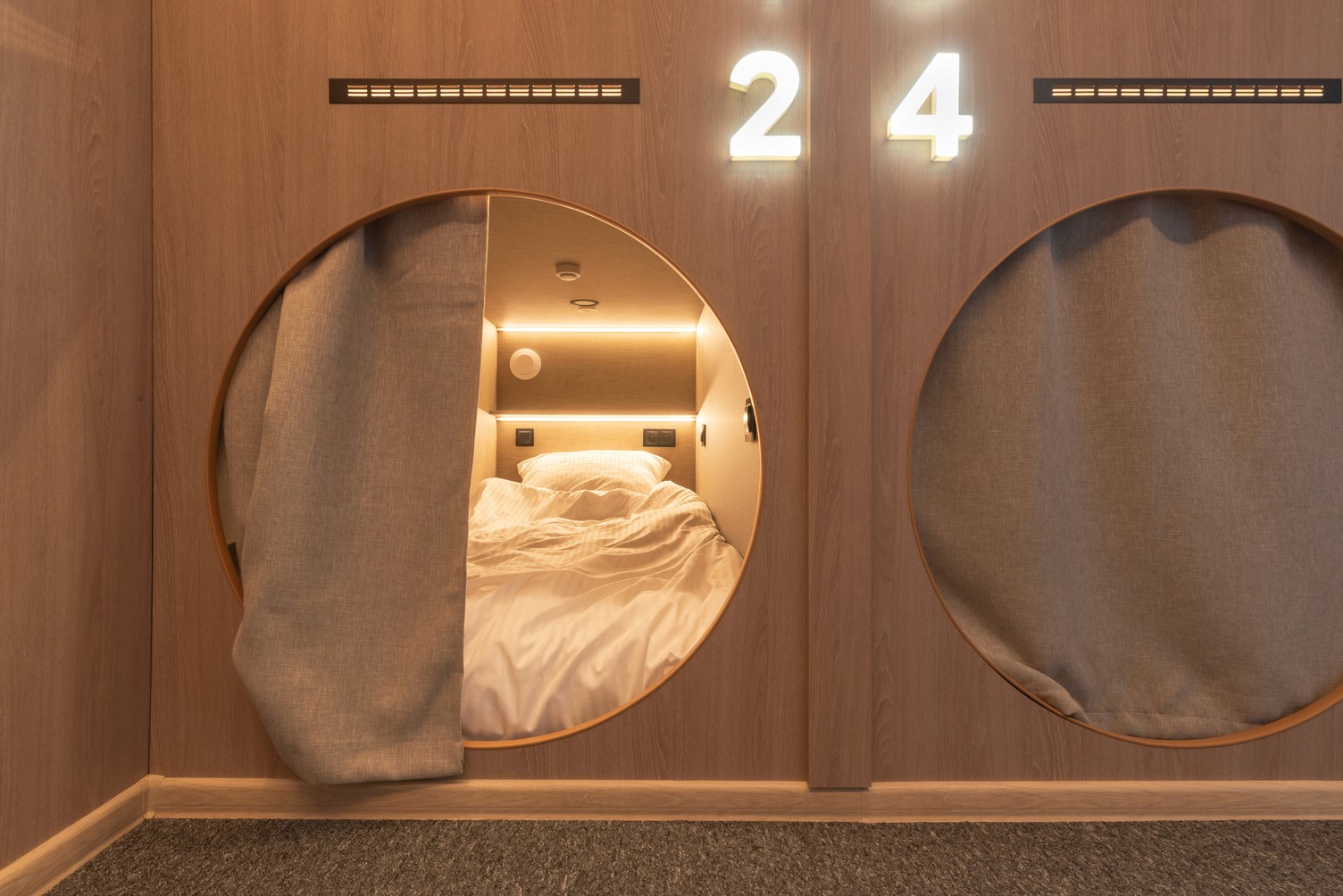 Capsule hotel rooms. Six wooden sleeping pods each with a bed, numbered 1-6. Interior of a hotel.