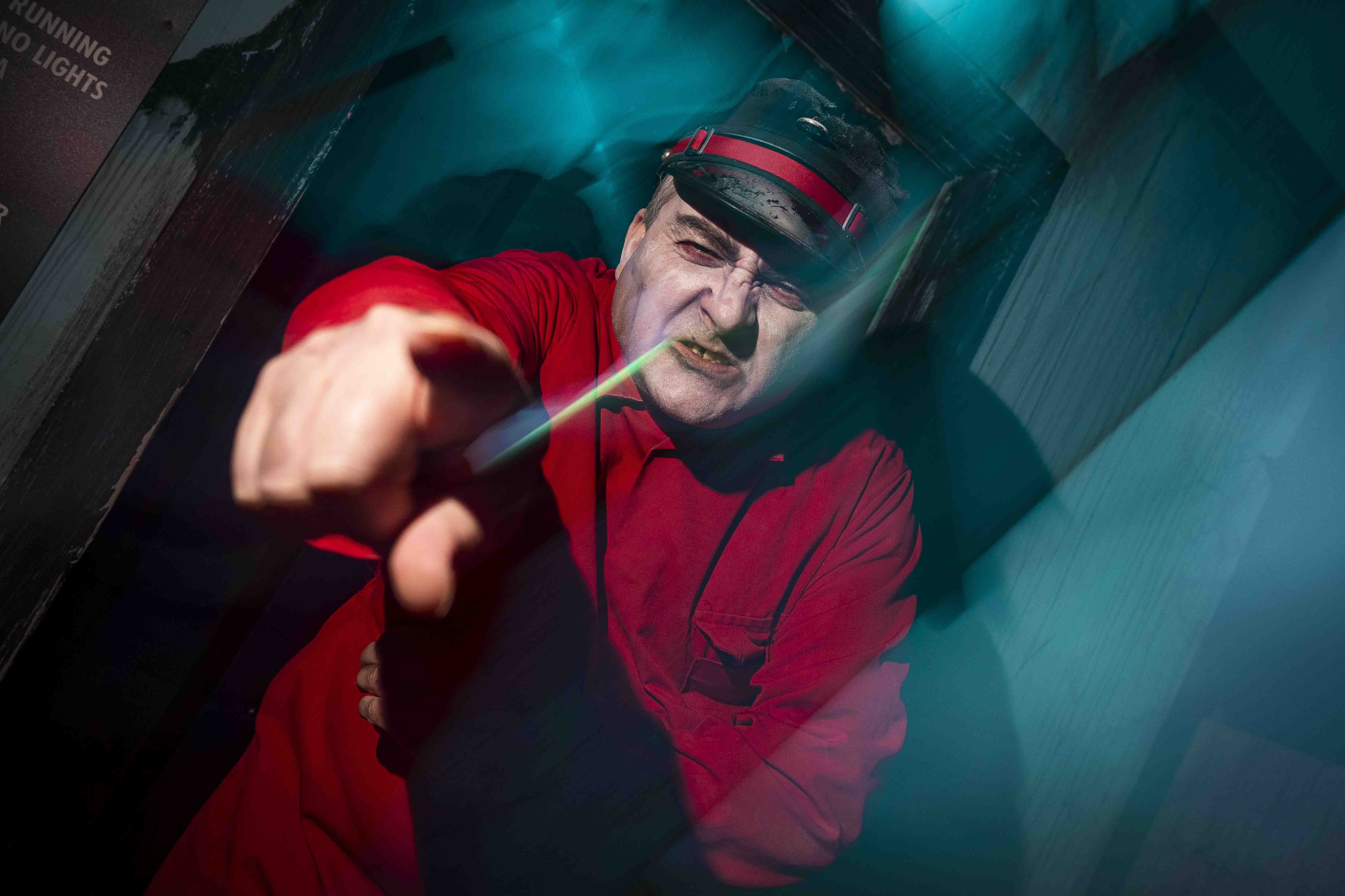 A man in a red shirt and hat points aggressively at the viewer.  He has a menacing expression, and the background is dark with blue light streaks.