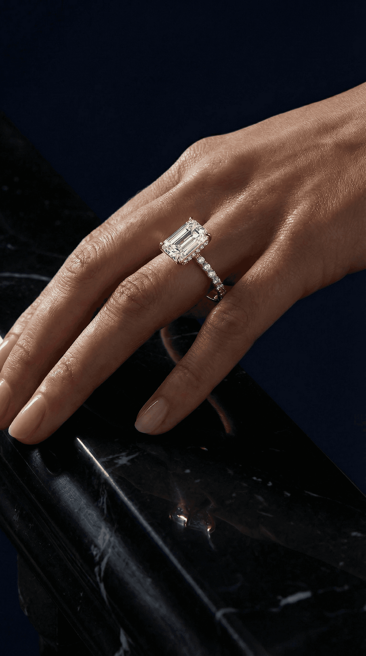 Emerald cut diamond engagement ring on hand resting on black marble surface