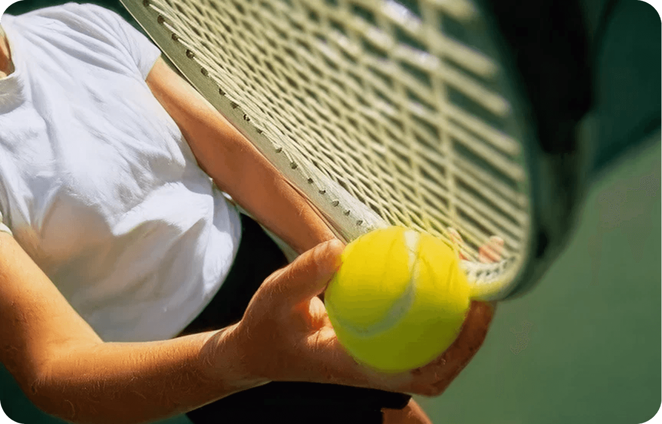 Tennis player holding a yellow tennis ball with a racket, ready to serve or return the ball.