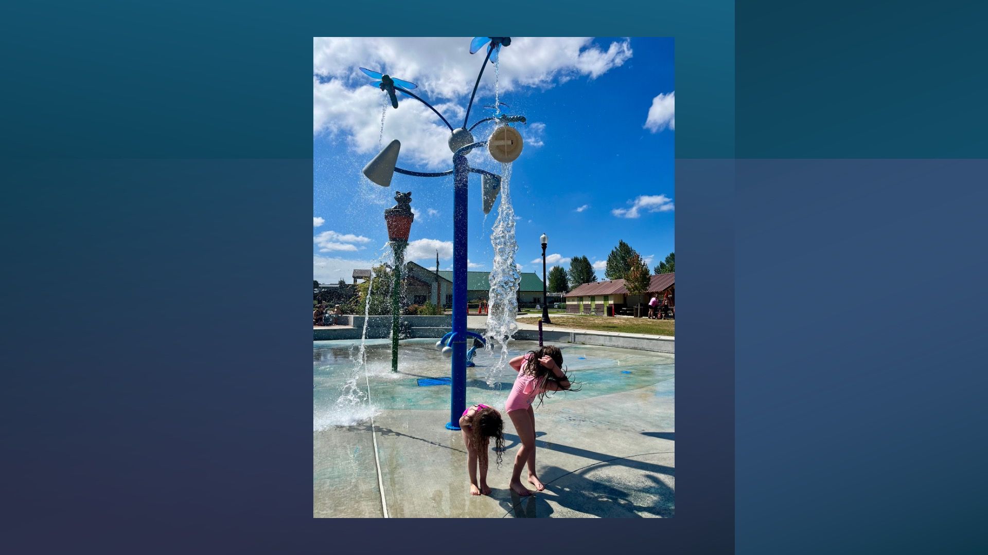 Children playing under water features at the Haller Park splash pad on a sunny summer day.