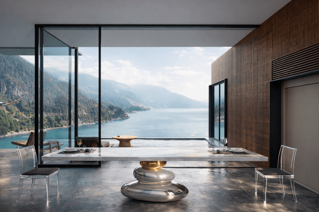Contemporary luxury dining space featuring a sculptural marble table with metallic base overlooking a panoramic lake view