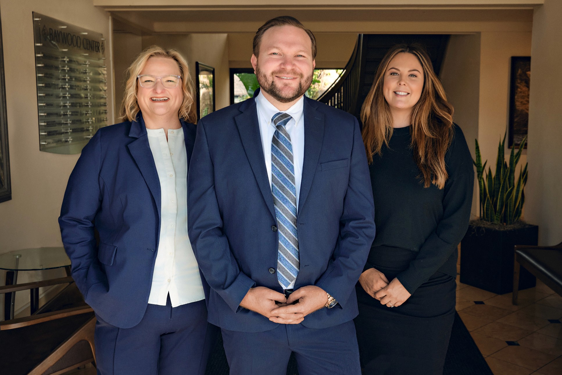 Law firm team photo with three attorneys smiling in office lobby setting