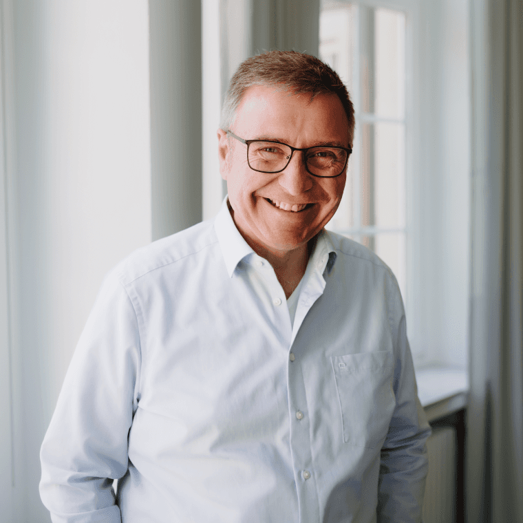 Älterer Männlicher Geschäftsführer im hellen Hemd steht locker vor einem Fenster im Büro von SLB.