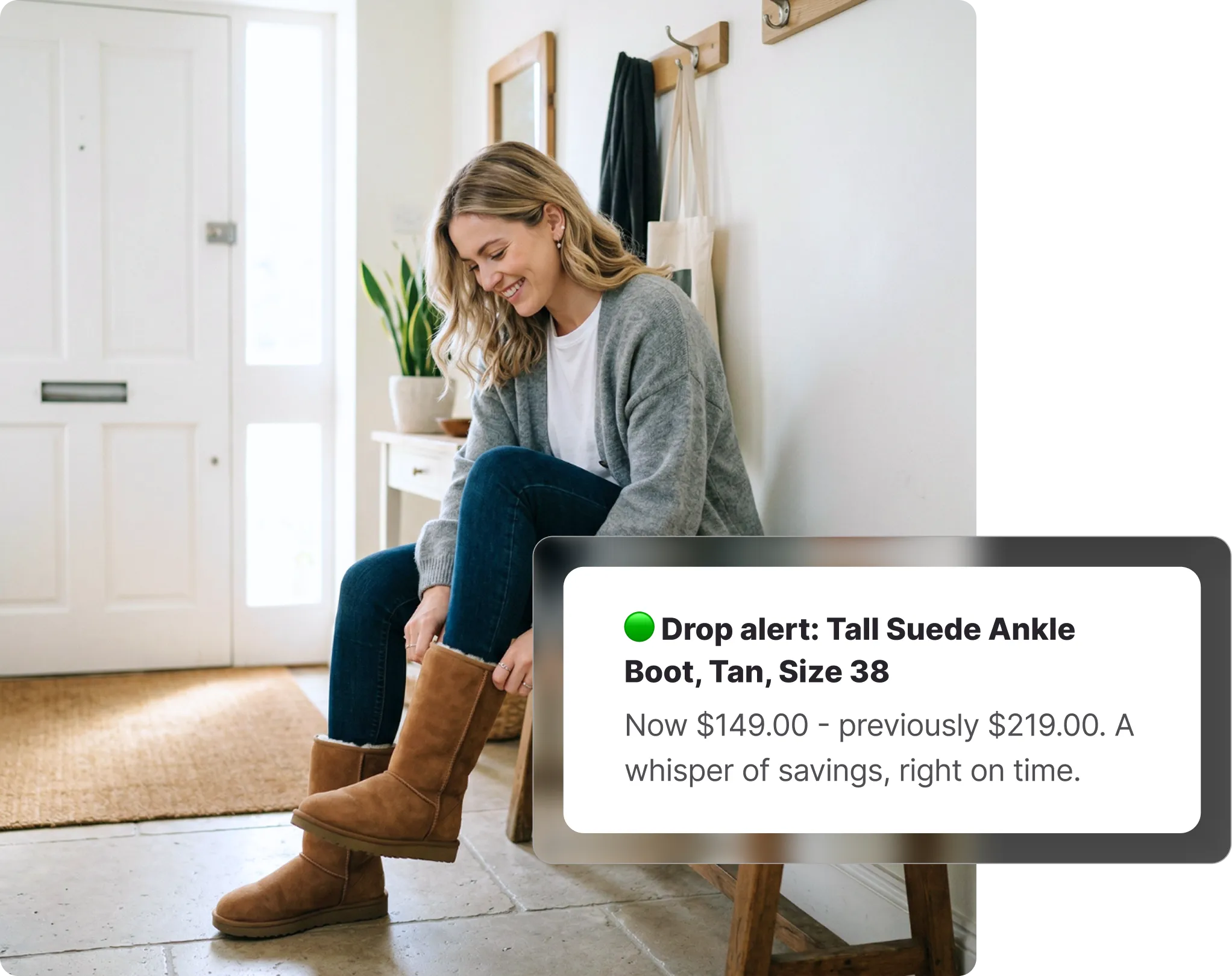Woman sitting in a hallway smiling while putting on tall tan boots, receiving a The Iconic price drop alert on Whisprice, with a grey cardigan and tote bag hanging on hooks behind her.