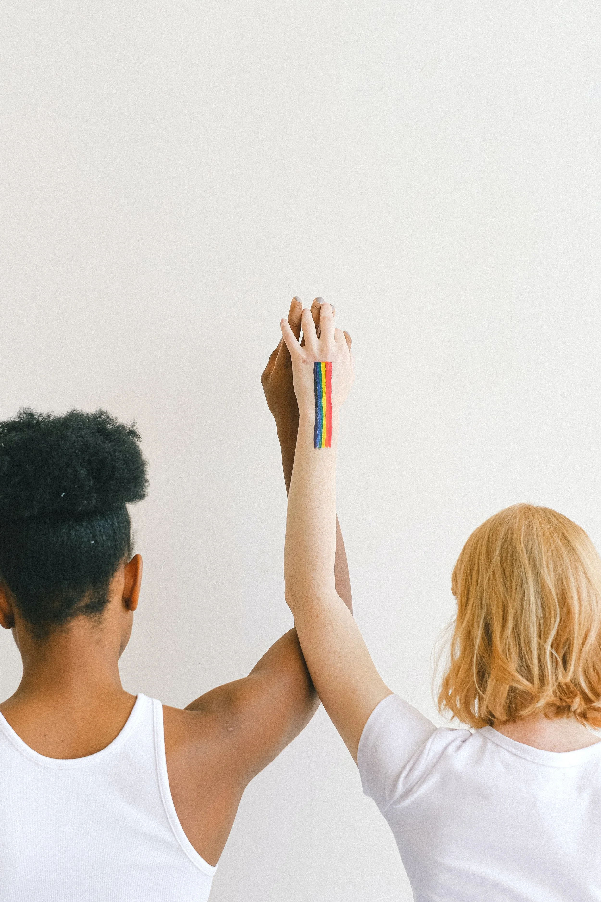 Two people proudly hold up their hands with the Pride rainbow painted on their wrists