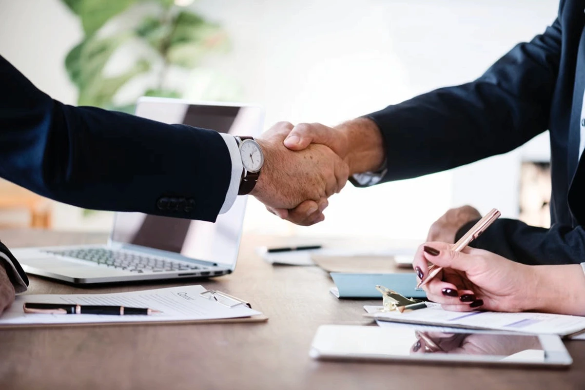 2 businessmen in shuits shaking hands over a table