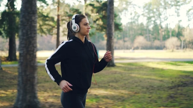 Woman walking outdoors in nature while listening to music on headphones