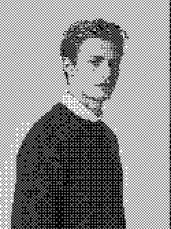 A young man in a dark sweater is standing sideways, looking over his shoulder against a plain background.