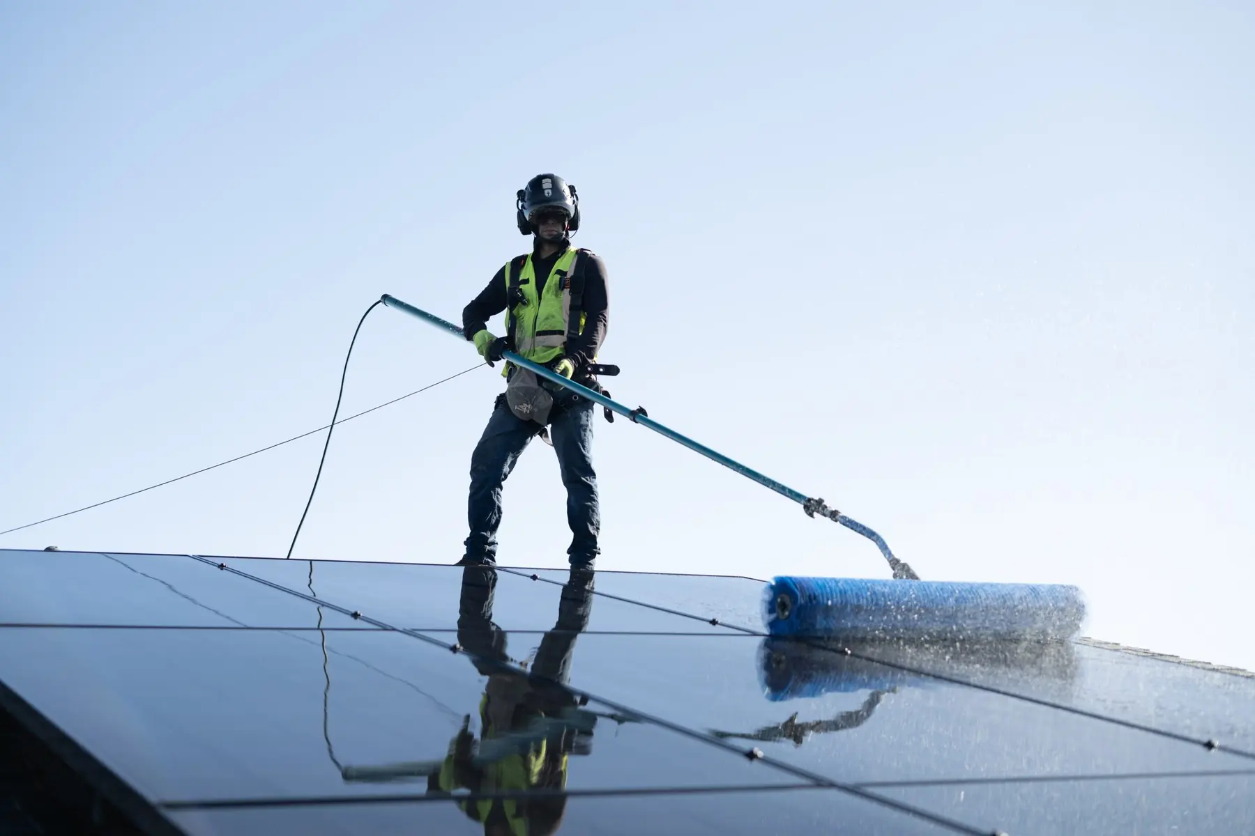 Technician with a soft pole brush, reflection on wet glass | Premier Solar Service, serving Central Valley, CA