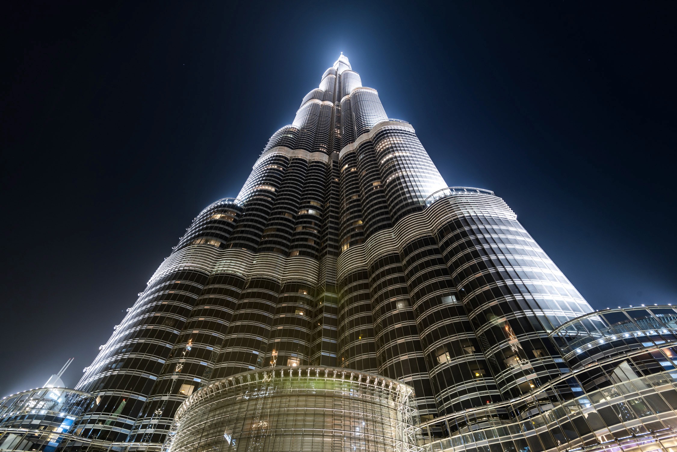 The Burj Khalifa skyscraper towers into a dark night sky, illuminated with interior lights and a bright peak.