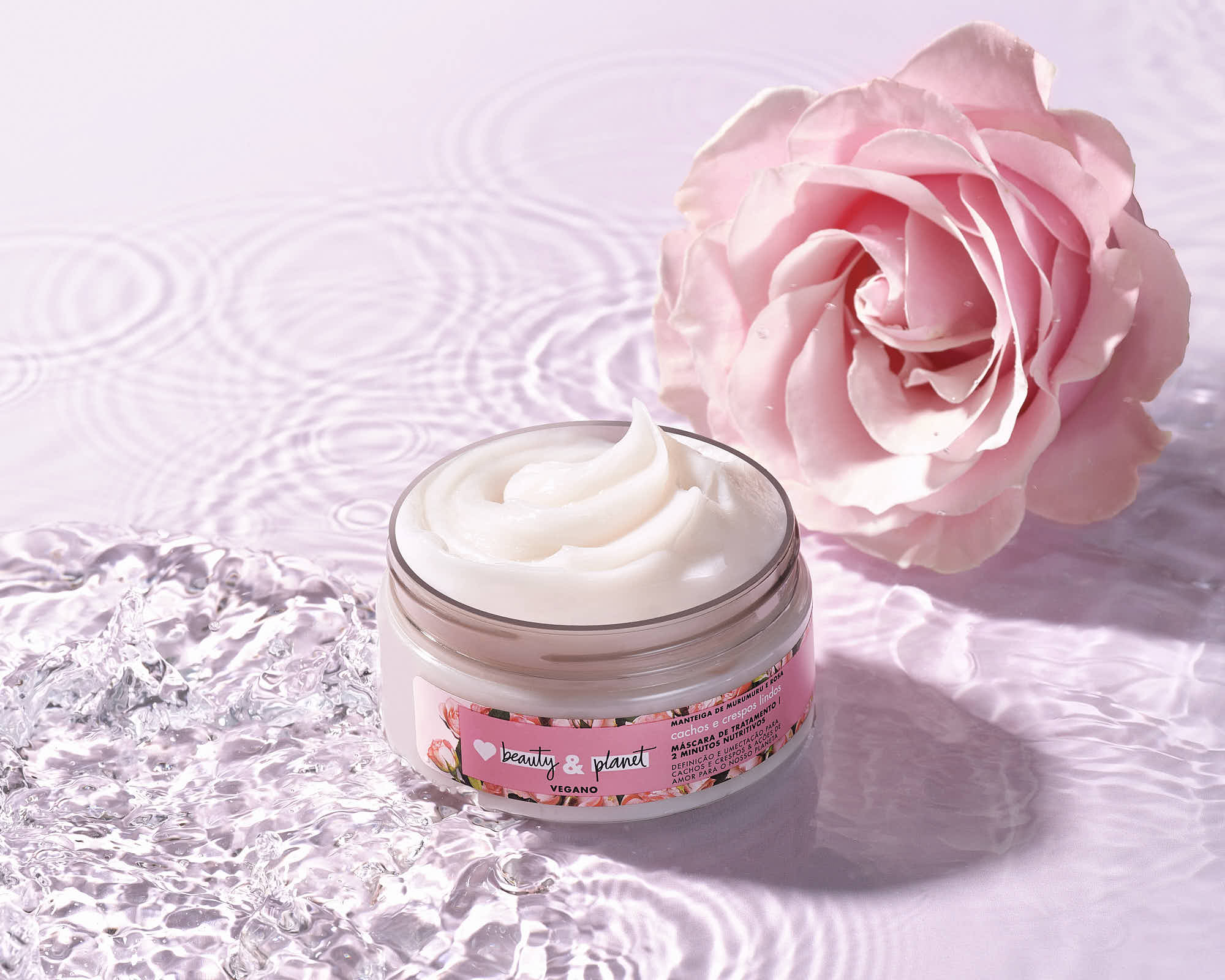 A small jar of cream sits next to a pink rose on a textured surface, evoking a soft, delicate ambiance.
