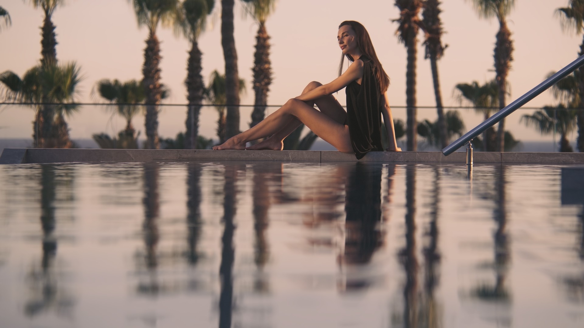 A woman is relaxing by the polol during the sunset