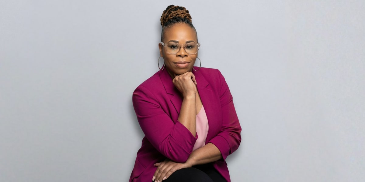 Dr. Renair Amin Shannon confidently seated, wearing a pink blazer, promoting the idea that life after 50 is empowering.