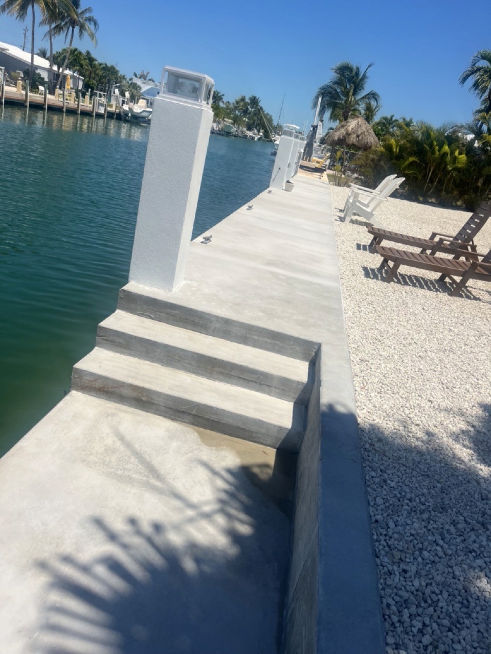 A serene outdoor seating area with two chairs, surrounded by lush greenery and a glassed-in structure.