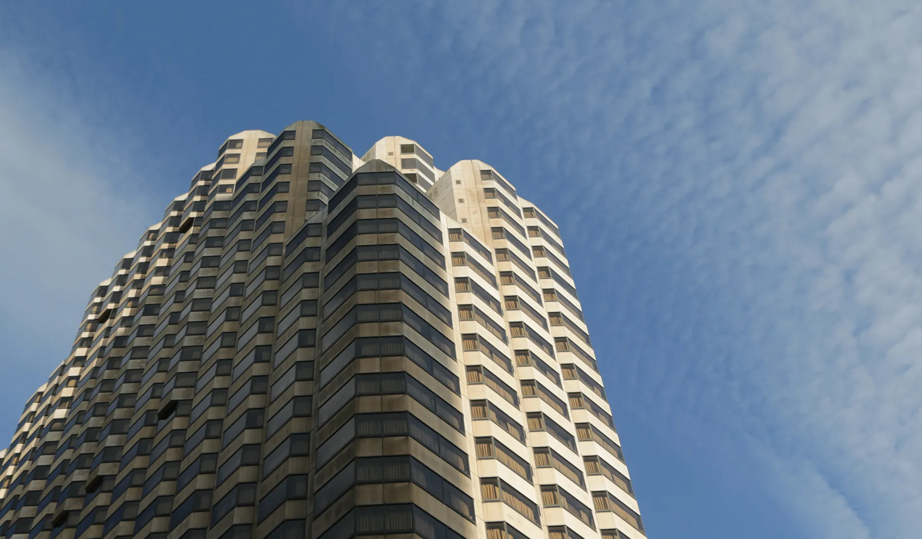 Low angle view of a tall residential skyscraper with a textured facade reaching toward a clear sky.