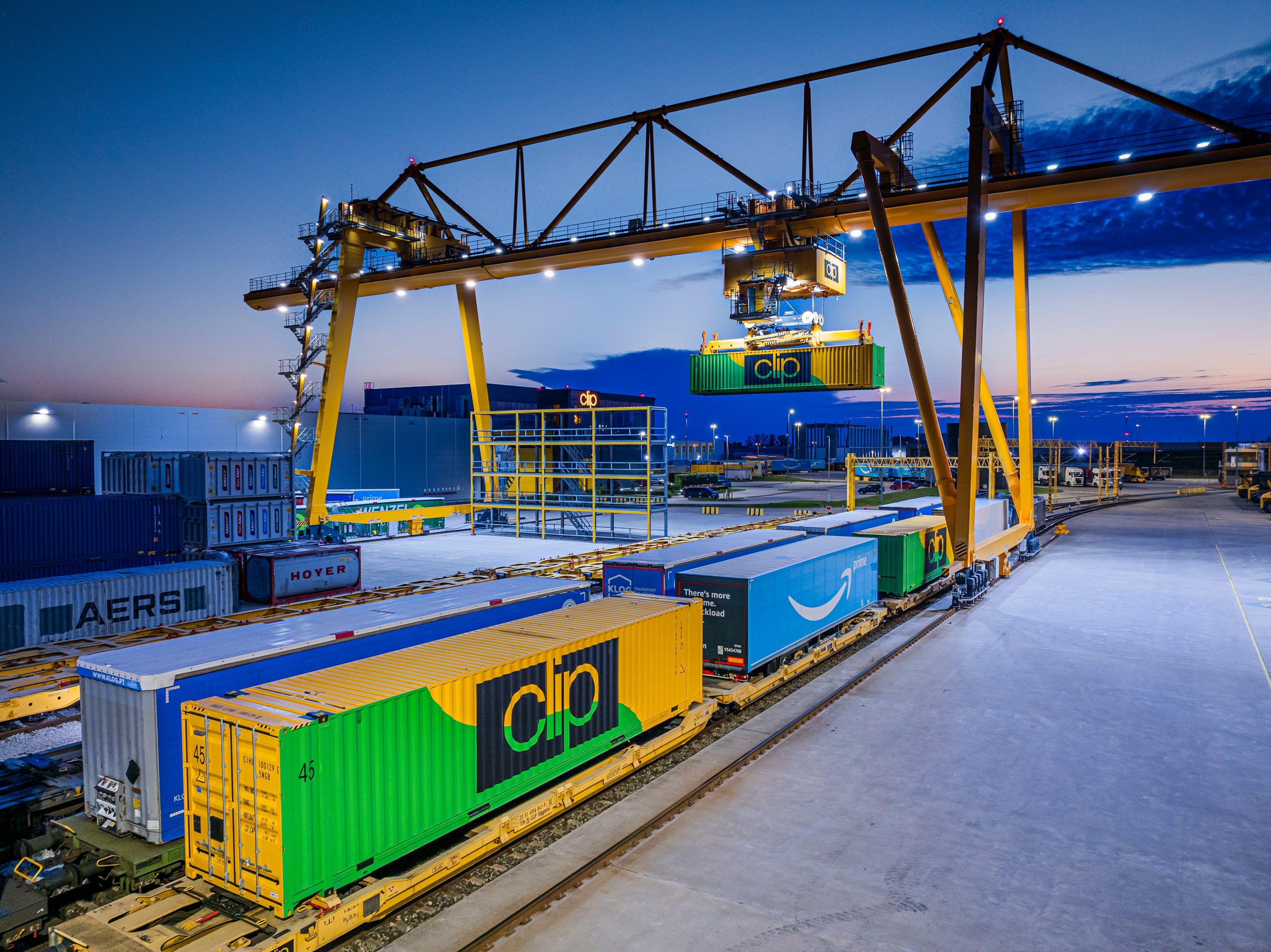 Gantry crane loading containers onto a train at dusk.