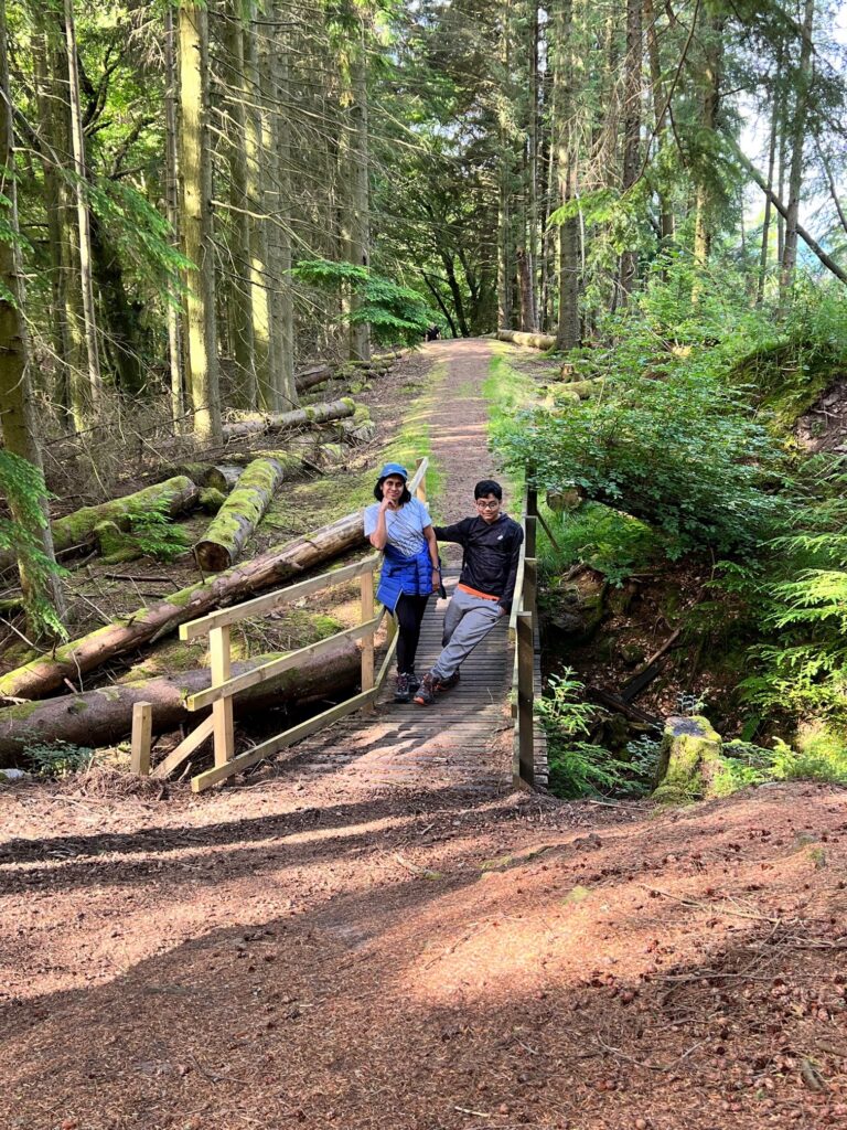 A bridge in the woods and two people posing for a photograph on the bridge. At Callander Crags