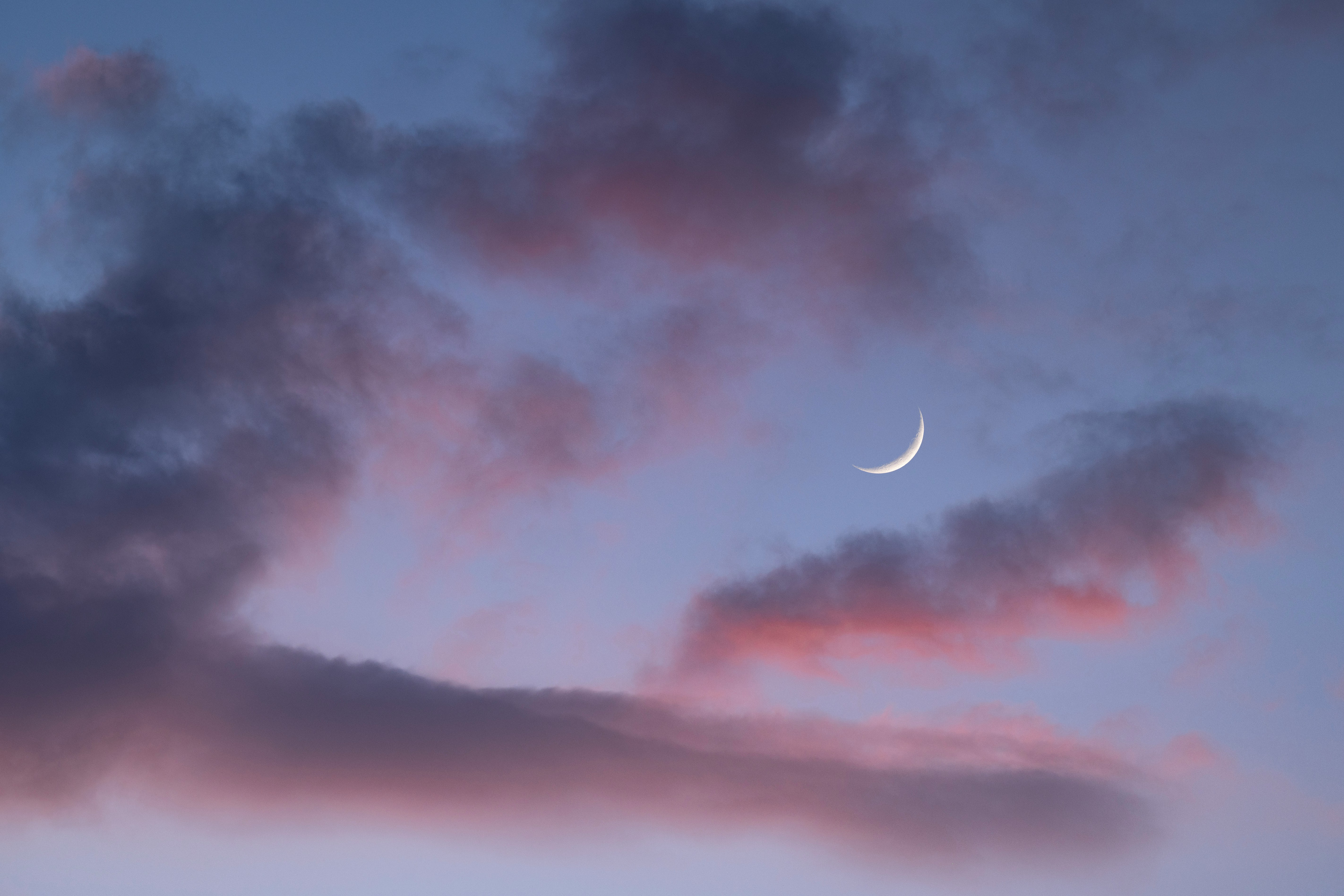 Crescent moon in a serene twilight sky with clouds.