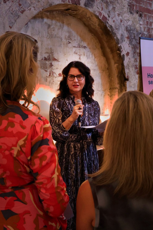 woman faces camera, speaking to a crowd holding a microphone