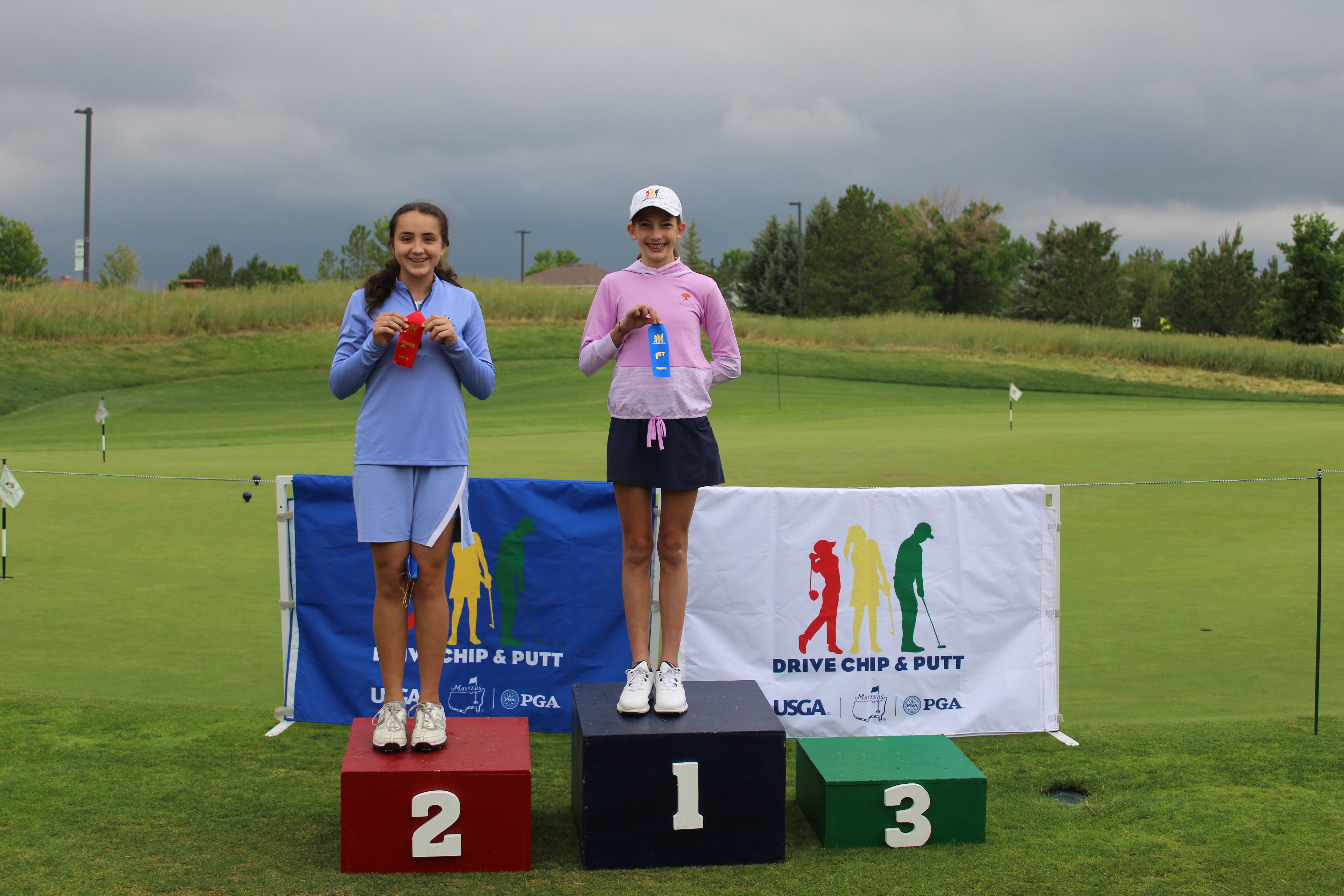 A group of students at the edge of a green, chipping balls towards net targets.