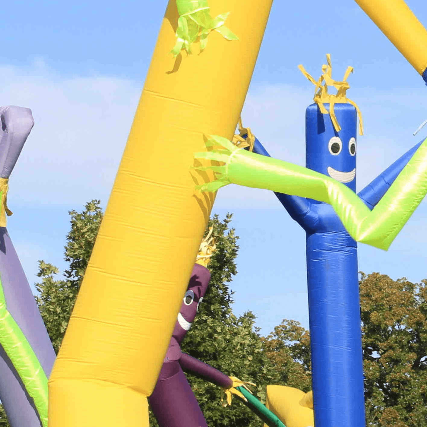 Colorful inflatable tube men dance in the wind against a clear blue sky.