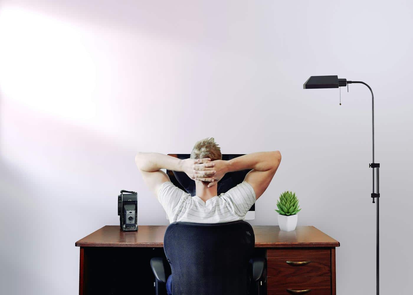 Man sitting on desk doing posture exercies by holding the back of his head with elbows stretched out