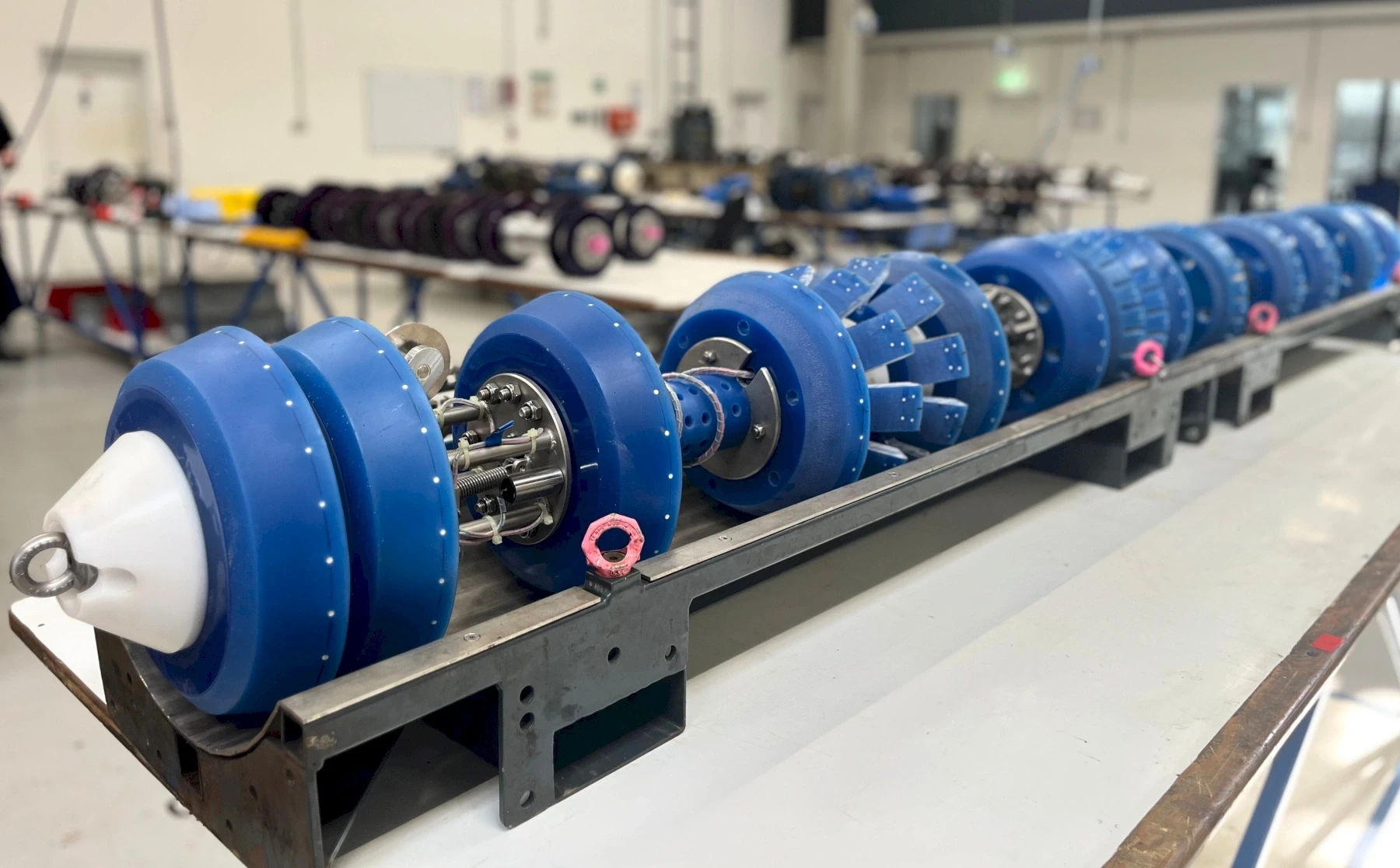 Close-up of industrial machinery: cylindrical blue parts, arranged on a metal rack. One white cone shape in the front.