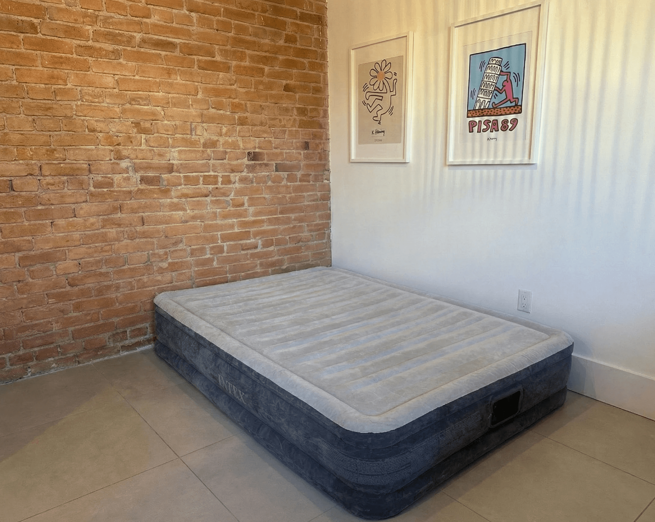 Matelas gonflable Intex double gris clair installé dans une pièce avec mur de briques et affiches encadrées à Montréal.