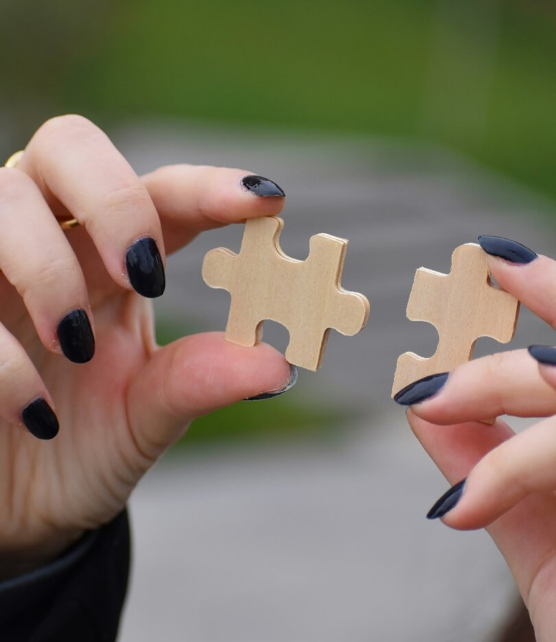 Hands with black nail polish holding puzzle pieces, symbolizing problem-solving and teamwork.