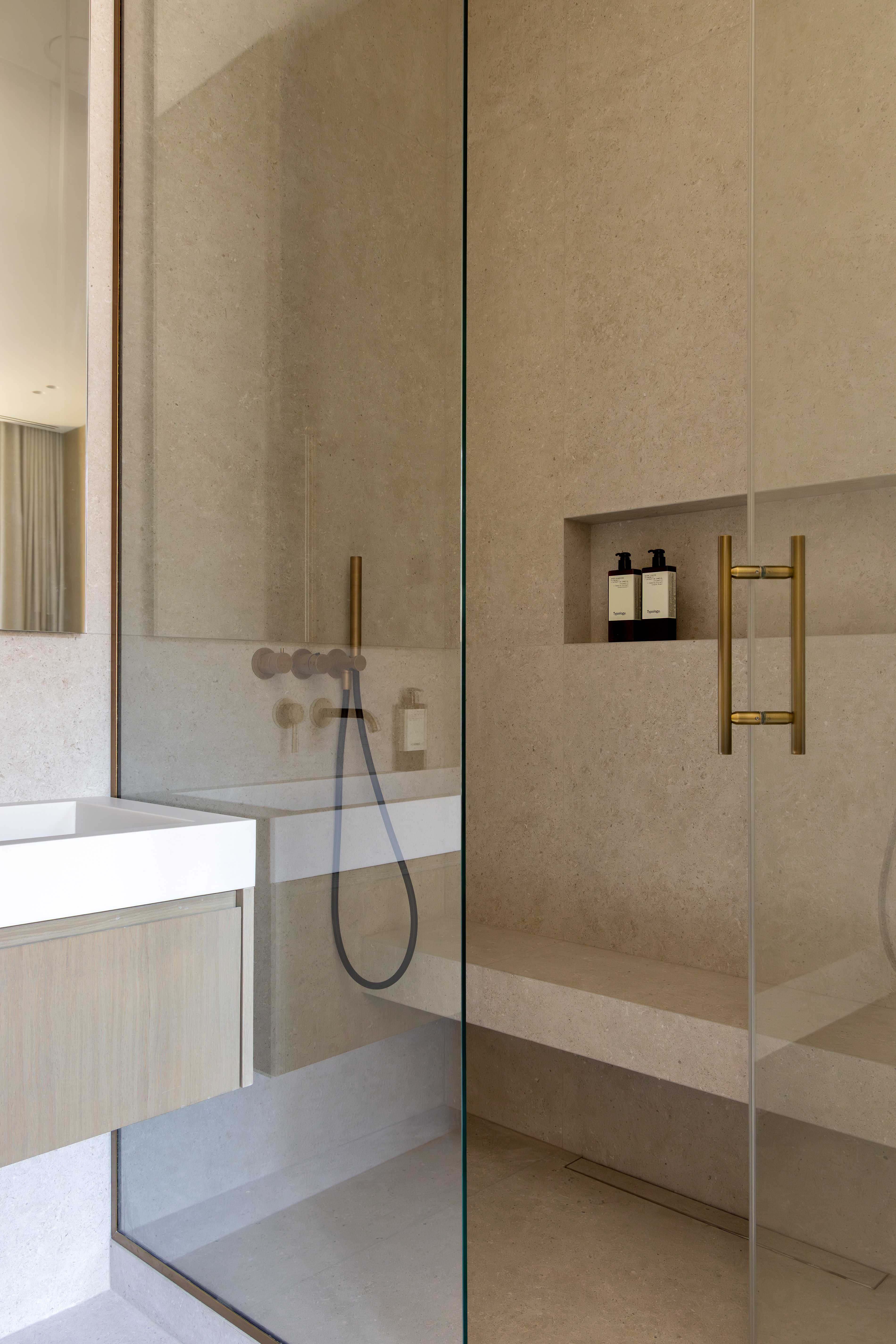 Salle de bains avec douche italienne en pierre, paroi vitree, robinetterie doree et niche pour produits