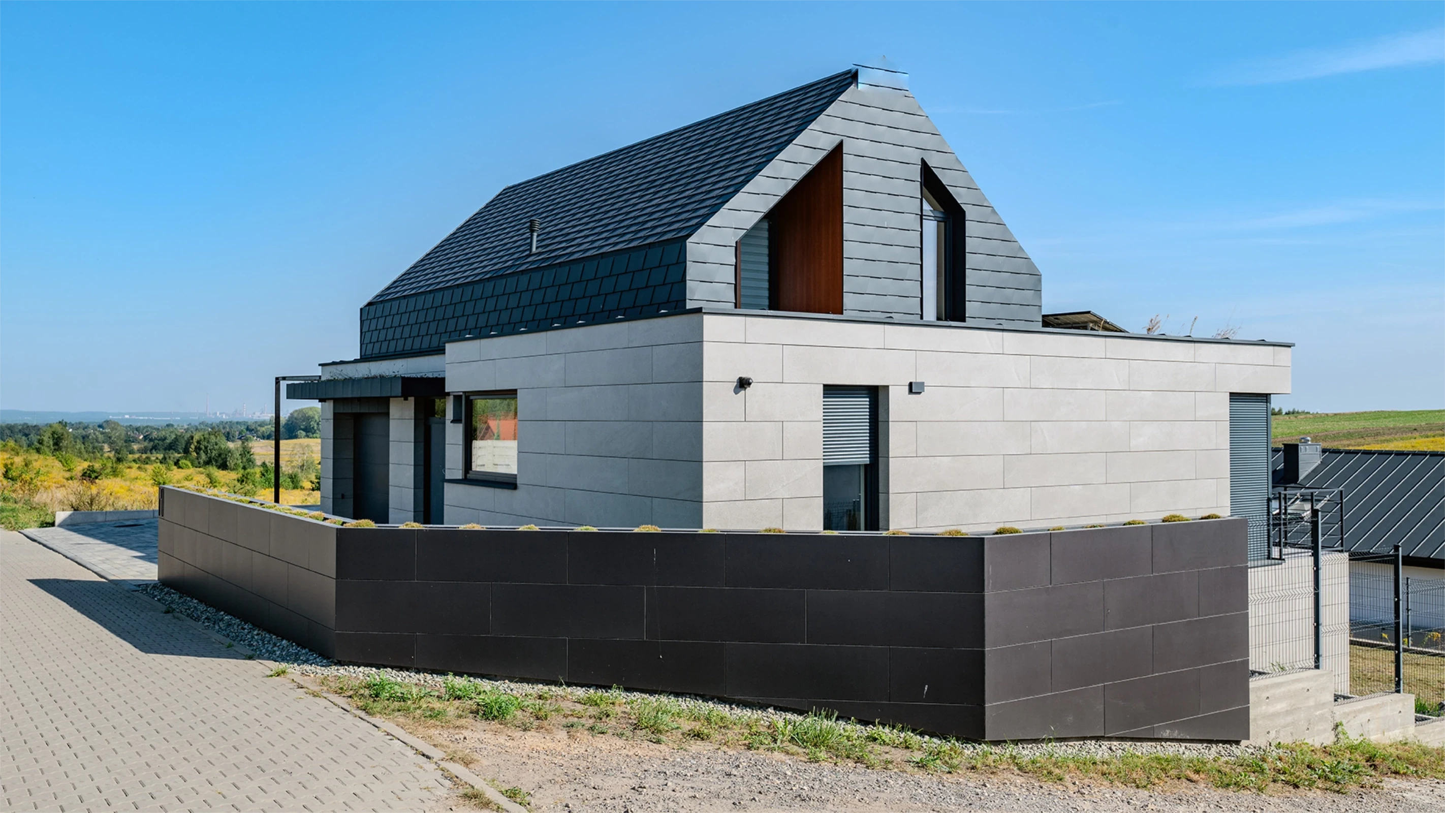 Nowoczesny dom z szarym dachem i elewacją. Ozdobiony czarnym płotem i oknami. Piękny dom na wzgórzu, w pogodny dzień.