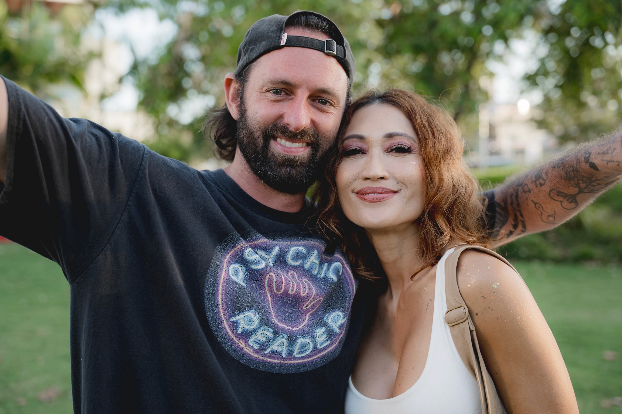 A couple smiling close together for a selfie at golden hour, tattoos visible on the man's arm.