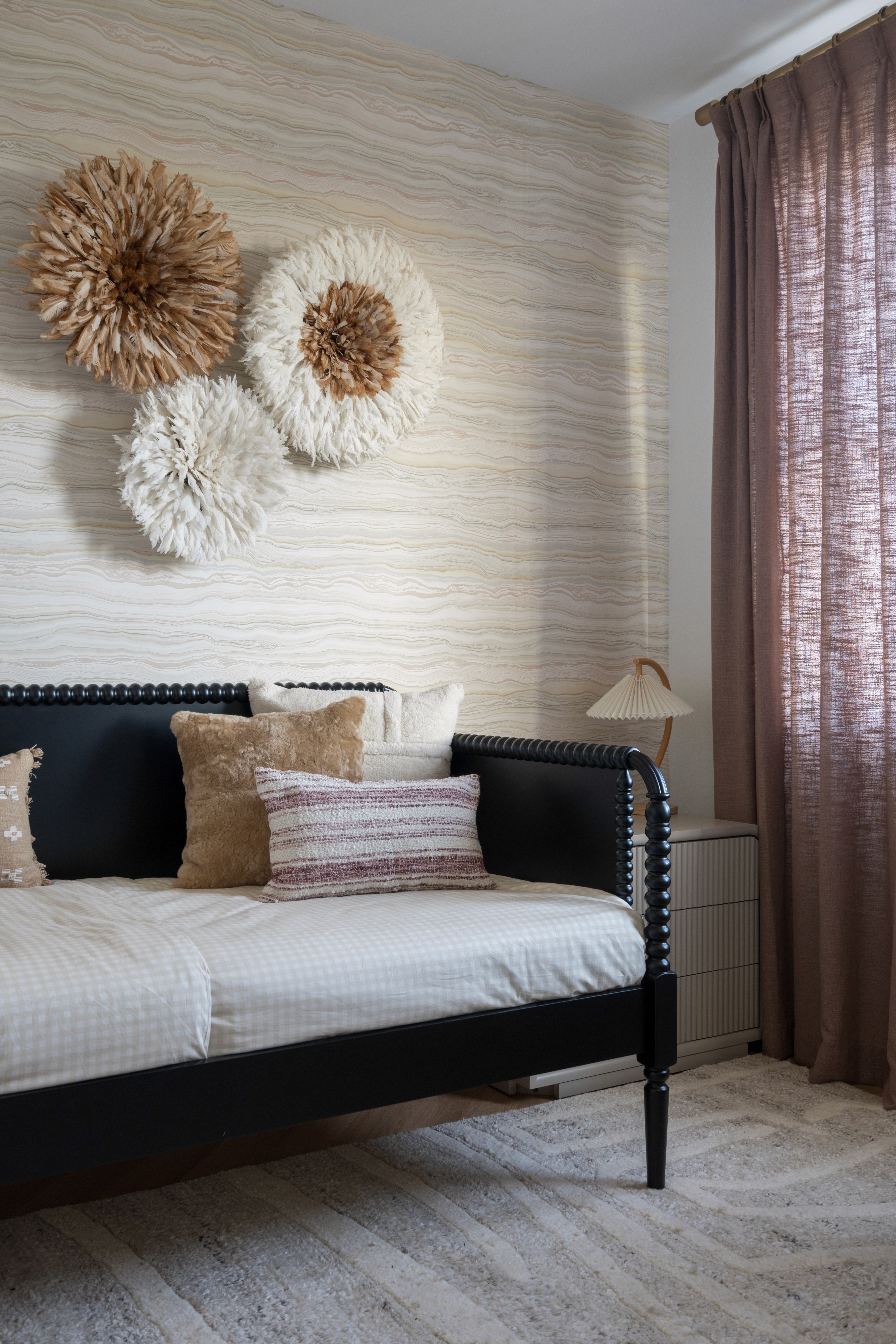 Black, wood framed day bed, light pink gingham bedding, pink and neutral colored throw pillows, paper flower wall art, and  patterned wall paper