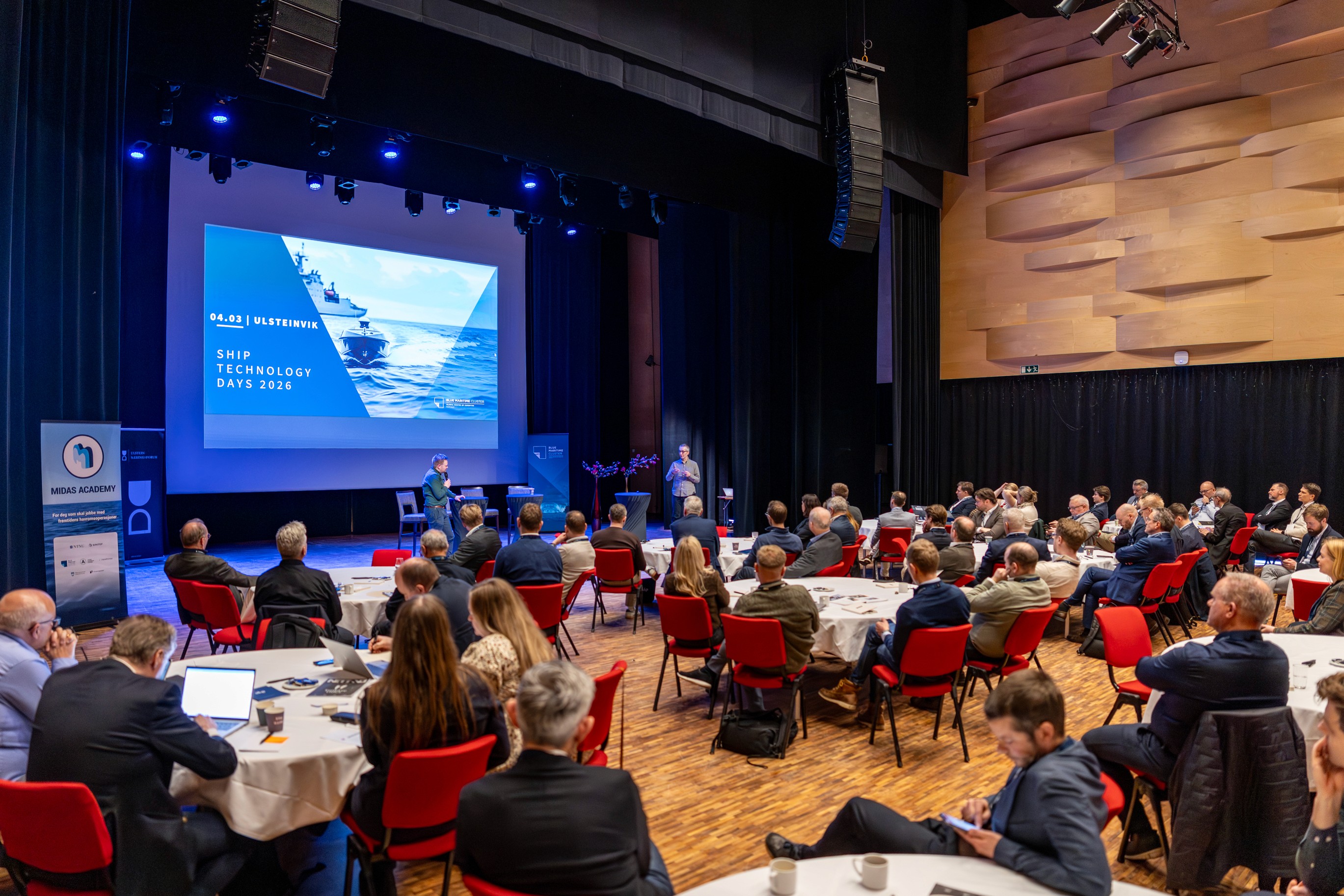 A person wearing a virtual reality headset stands in front of multiple screens, engaged in a digital experience.
