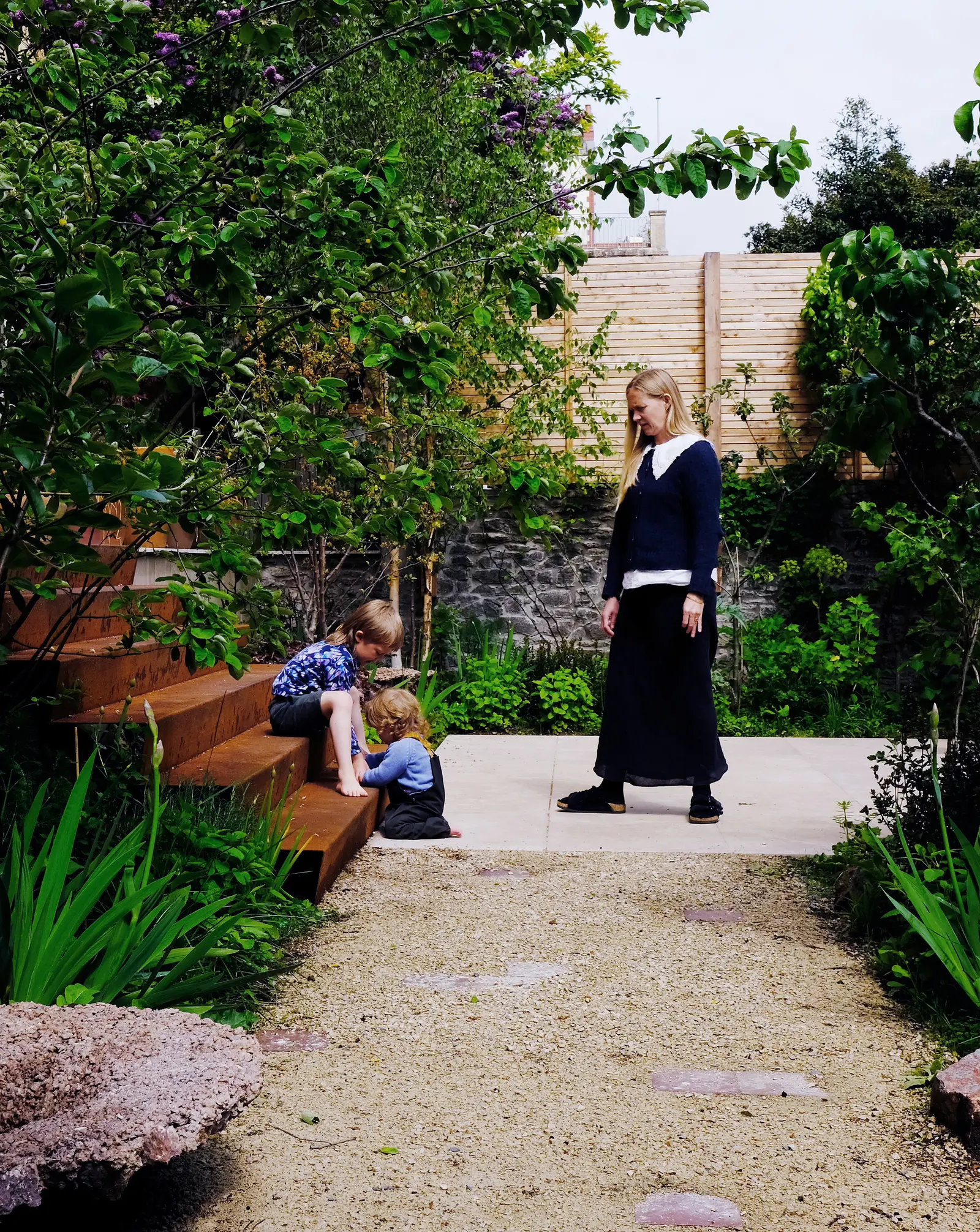 A person in a garden setting with greenery, pathways, and stone features, creating a peaceful atmosphere.