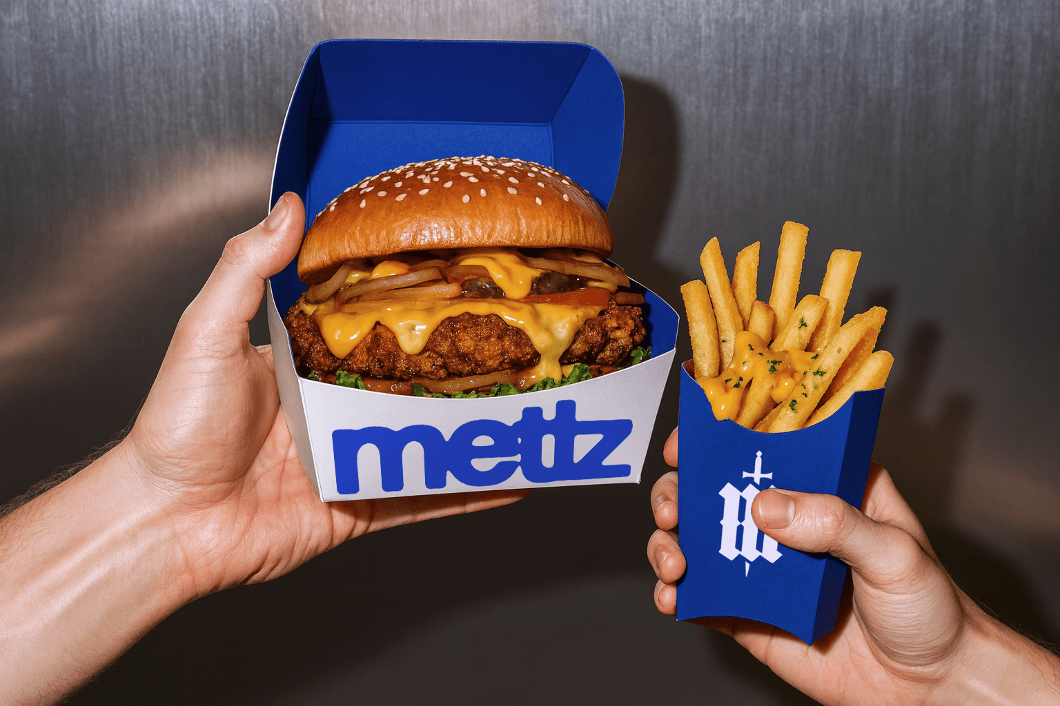 Hands holding a fried chicken burger in a branded Metz box and a serving of fries with cheese sauce in a blue container.
