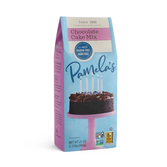 Front of box packaging for Pamela’s chocolate cake mix featuring a whole single-layer dark chocolate cake with swirls of dark chocolate frosting on top and lit birthday candles on a pink cake pedestal.