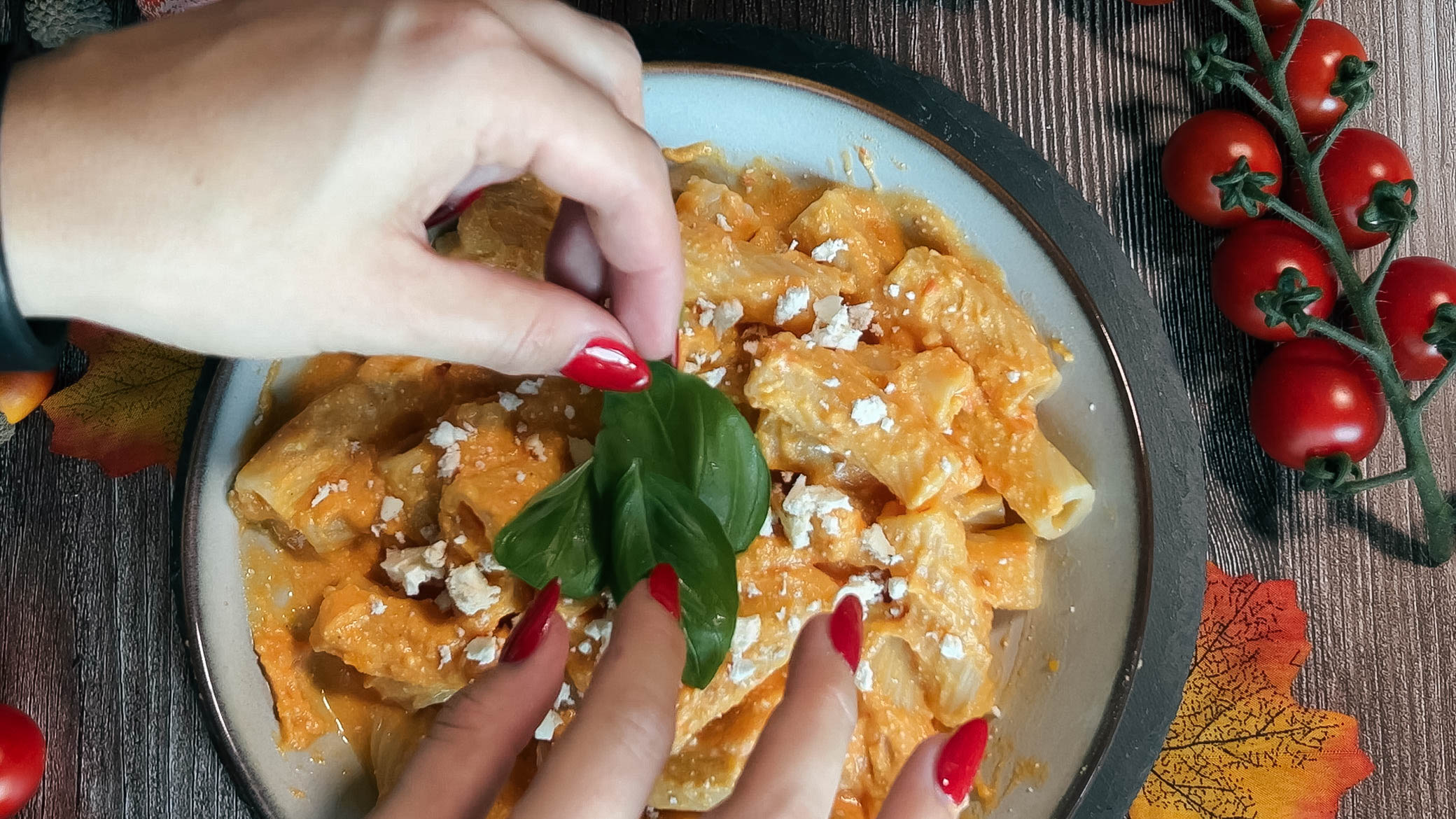 Servieren der Kürbis-Feta-Pasta mit frischem Basilikum. Saisonal herbstliches Gericht, dekoriert mit Cherrytomaten und gesunden Zutaten.